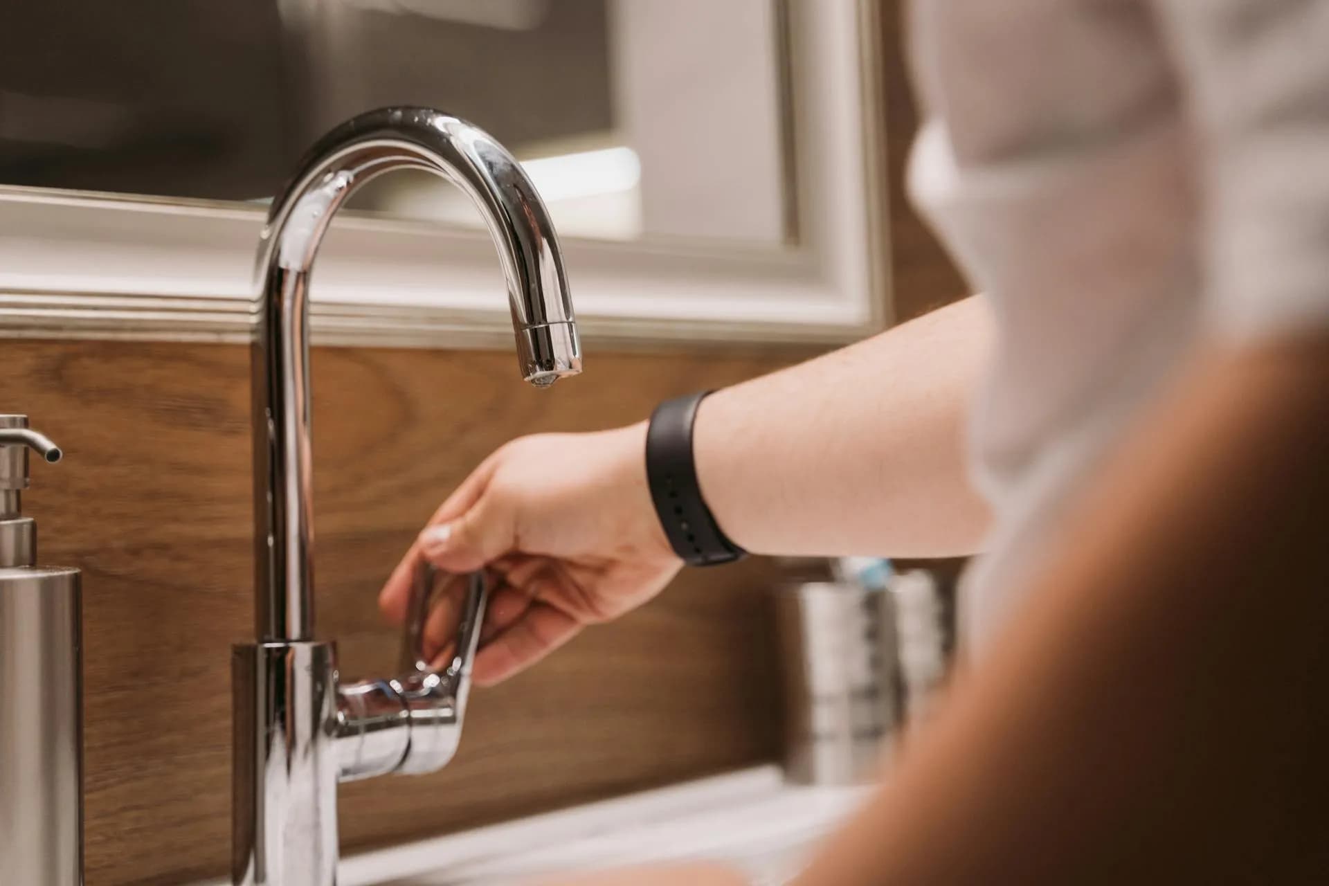 Hand adjusting a modern, chrome-finished faucet in a bathroom with wooden details.